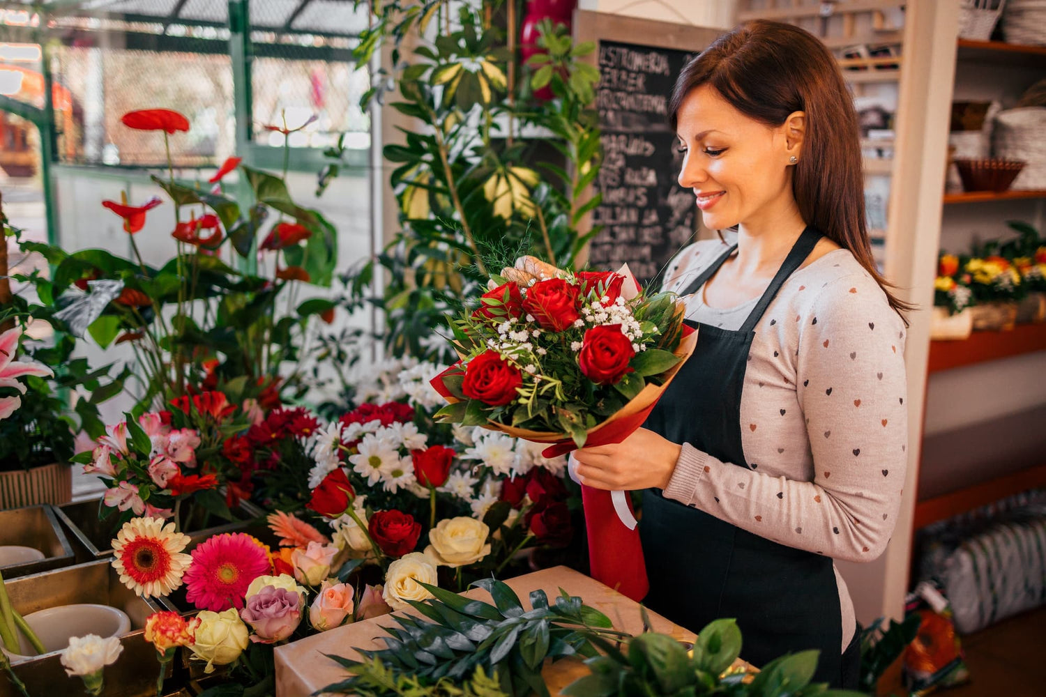 Florist holding a bouquet with roses, while standing surrounded with flowers at florist shop.